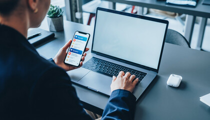 Businesswoman using laptop and holding smartphone with social media notification, modern office workspace, digital communication, technology, and productivity concept