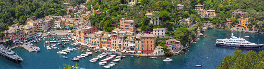 Panoramic photo of Portofino harbor with boats, buildings and green hills in Italy, Liguria region