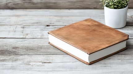 Fototapeta premium Leather journal on wooden table with potted plant, creating serene workspace atmosphere