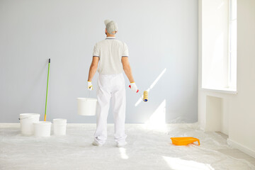 Back view of a man painter using a brush to paint a wall during home or apartment renovation. A...