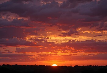 Warm glowing sun dips below dark tree line as fiery orange and red clouds fill sky creating dramatic natural scene. ideal for travel nature or mood based projects