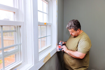 Fototapeta premium Handyman is carefully sanding wood trim next to window in well lit room on task, preparing for painting finishing in home improvement