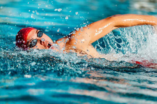 Swimming man. Swim competition swimmer athlete doing crawl stroke in swimming pool. Sports man male swimmer with goggles and cap breathing racing in indoor stadium. Speed exercise workout.