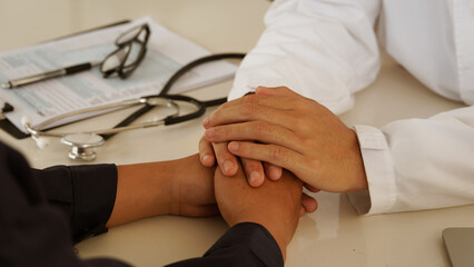 Doctor comforting and supporting patient by holding hands during medical consultation showing care...