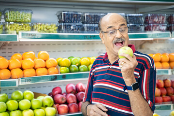 Fototapeta premium Senior indian man showing green apple fruit at fruit shop. Healthy lifestyle concept.