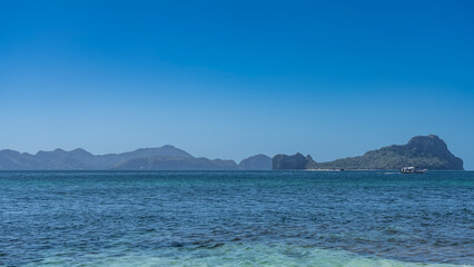 Beautiful tropical seascape. Aquamarine turquoise water. Ripples on the surface of the sea. Bangka  boat floats in the distance. Mountains on the horizon. Clear blue sky. Copy space. Philippines.