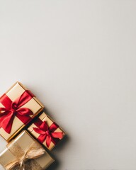 Close-up of elegant luxury Christmas gift boxes wrapped in gold and red paper with satin ribbons, placed on white minimal background with soft shadows, festive and stylish composition