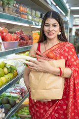 Indian woman in traditional saree, holding vegetables bag after purchasing at super shop.