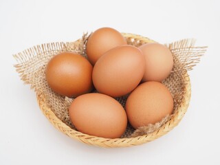 Several fresh chicken eggs are placed in a basket on a white background.