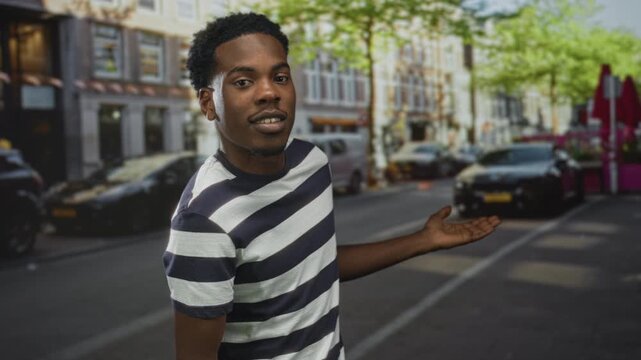 Man extends hand toward parked cars on busy street framed by city buildings and sunlit trees; invitation.