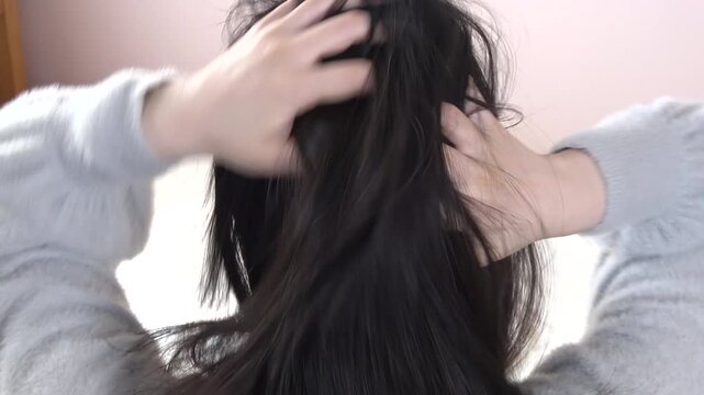 黒髪の頭を掻く女性の後ろ姿のクローズアップ 