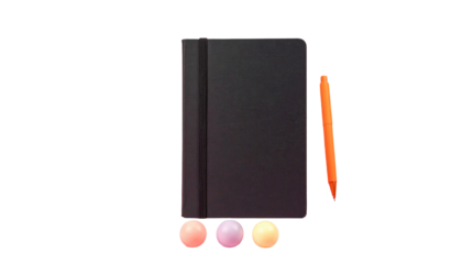 Black, closed notebook next to an orange pen and three gumballs, isolated on black