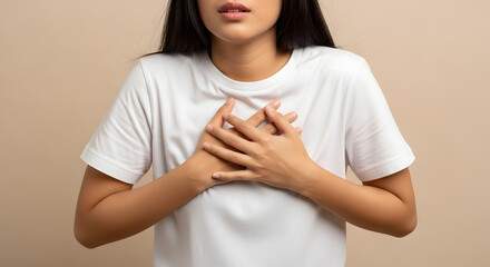 Young woman clutching chest in discomfort or pain, Mid-close-up of female experiencing chest pain, Woman holding hands over chest against neutral background, Studio shot conveying distress and health 