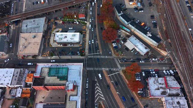 A high angle, aerial view of a busy intersection by Long Island Railroad elevated train tracks on Long Island. Taken on a cloudy day. the camera is stationary.