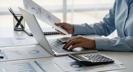 Financial report analysis tax budget financial accounting specialist reviews printed charts desk while entering data laptop and calculator showing focused planning and organized office workflow