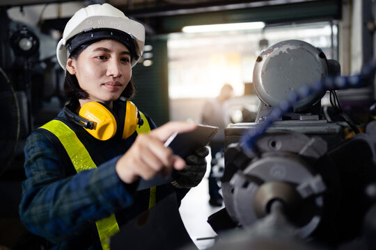A woman in a yellow vest and a hard hat is working on a machine