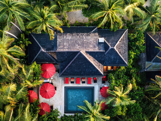 Aerial view of a tropical villa surrounded by lush greenery and palm trees with a pool and red umbrellas creating a paradise retreat — generative AI