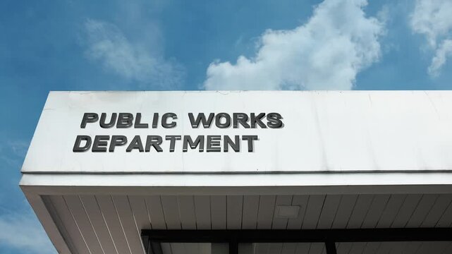 Public Works Department word sign displayed on a large governmental or civic building under a clear blue sky, symbolizing infrastructure, construction, maintenance, community services