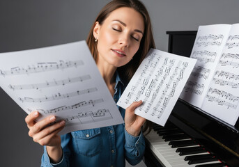 Focused young woman practicing piano, holding and analyzing sheet music for classical composition at upright keyboard in serene atmosphere