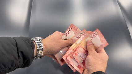 A close-up of a man's hands counts a bundle of bills for five thousand Russian rubles. Man counts red paper 5000 rubles bills. Russian cash money in male hand. A man holds a wad of money in his hands. - Powered by Adobe