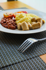Hotel healthy breakfast menu of mashed potatoes, omelette, read beans, tomatoes, and sausages served on a white plate