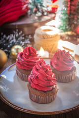 Delicious chocolate cupcakes topped with red buttercream, served on a ceramic plate with a warm festive atmosphere. Perfect sweet dessert for Christmas and New Year celebration.