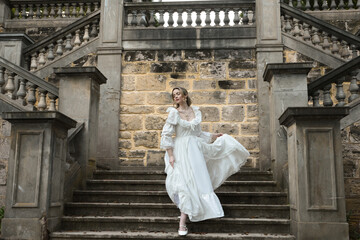 Naklejka premium Full length female figure of blonde model wearing white fantasy wedding gown. walking down stairs on historical staircase of fairytale castle location 