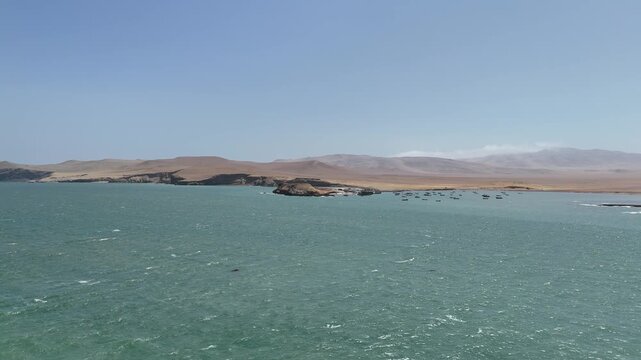 Moving forward captures a close-up view of the small fishing village and the elevated observation area at Playa Lagunillas cove in Peru's Paracas National Reserve