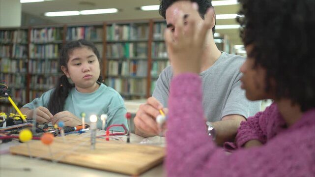 A teacher guiding students in a robotics project during a STEM class in the library