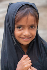 Smiling little girl wearing a black scarf looking at the camera with innocence and joy in a rural outdoor setting