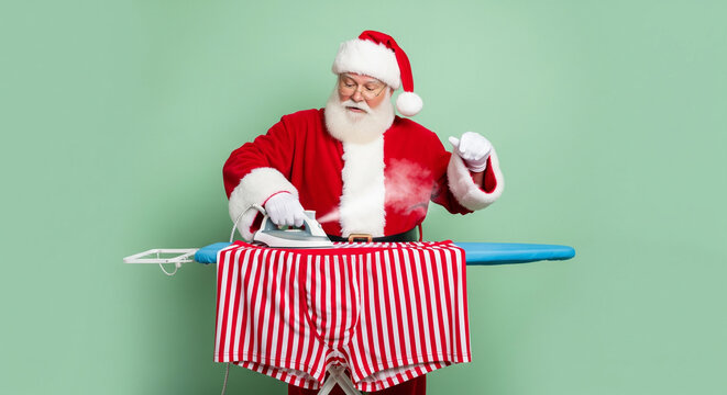 Santa Claus ironing his festive red and white striped boxer shorts with a steaming iron on an ironing board with a mint green background
