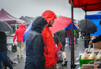 Couple looking at soy milk and tofu in the market stalls in the rain. Unrecognizable people with umbrellas shopping in the market.