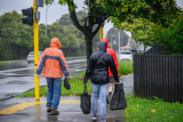 People carrying shopping bags and walking on the pedestrian footpath in the rain. Auckland.