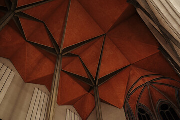 A low angle view of a striking red geometric vaulted ceiling supported by slender dark columns in a church interior.