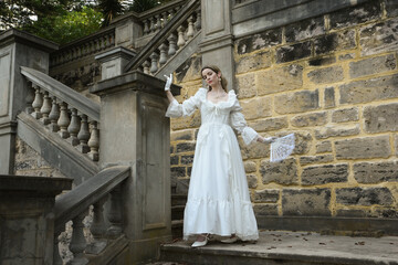 Obraz premium Full length female figure of blonde model wearing white fantasy wedding gown. walking down stairs on historical staircase of fairytale castle location 
