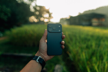 New smartphone in hand, green blurred background of rice fields in nature