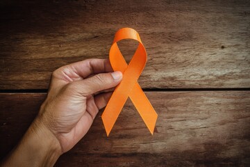 Hand holding an orange awareness ribbon against a wooden background, representing support for various causes