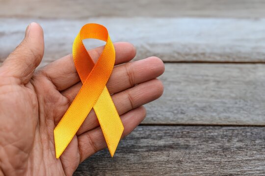 Hand holding an orange awareness ribbon, symbolizing support and hope for various causes, including suicide prevention or leukemia