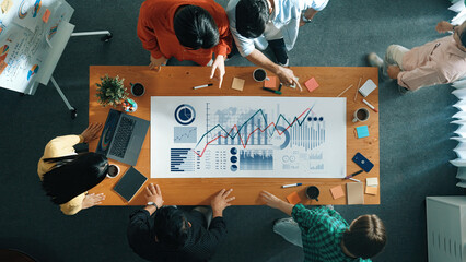 A diverse group of professionals engages in a collaborative business meeting, analyzing data insights and discussing strategies using charts and reports on a modern workspace table. Scalp