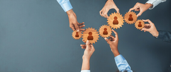 Hands come together to connect wooden gears, symbolizing teamwork, networking, and collaboration in a professional setting, promoting unity and shared goals. Amity