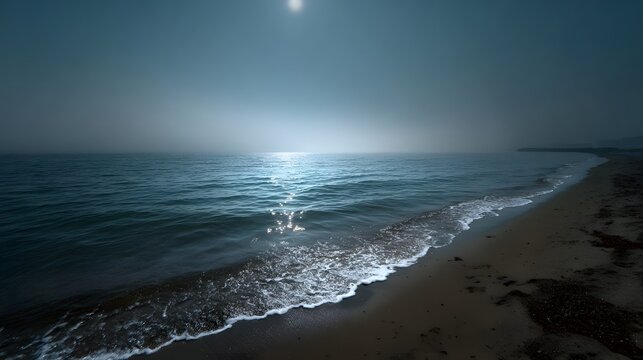 A serene beach scene at twilight with gentle waves lapping the shore under a misty sky illuminated by moonlight