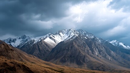 Dramatic mountain range with rugged snow capped peaks under a vast moody sky filled with dark stormy clouds