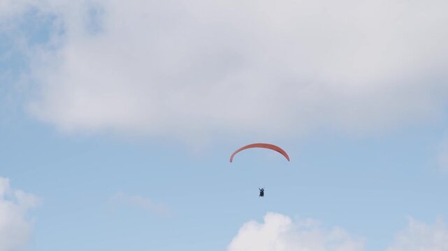 Flight of a red paraglider against the background of blue sky and clouds