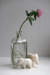 Minimalist retro style still life with a red clover flower in a glass vase and two small toy elephants.