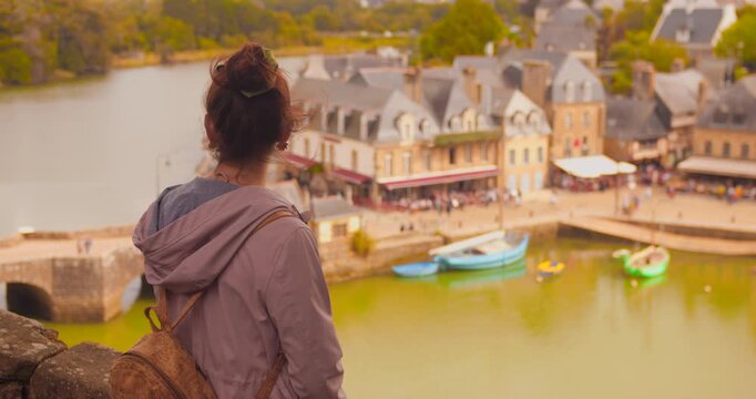 High-angle view of a woman looking out over the serene Saint-Goustan port in Auray, France. The scene captures the charming boats and historic buildings, evoking a peaceful atmosphere.