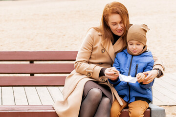 Happy Mother and Son Holding a Handmade Paper Boat Together in Autumn Park