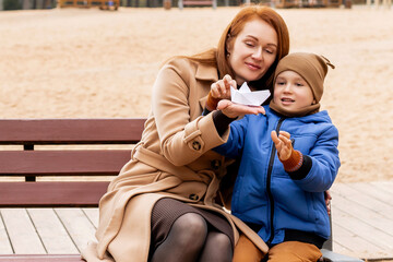 Happy Mother and Son Holding a Handmade Paper Boat Together in Autumn Park