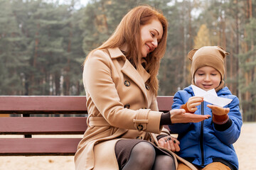 Happy Mother and Son Holding a Handmade Paper Boat Together in Autumn Park