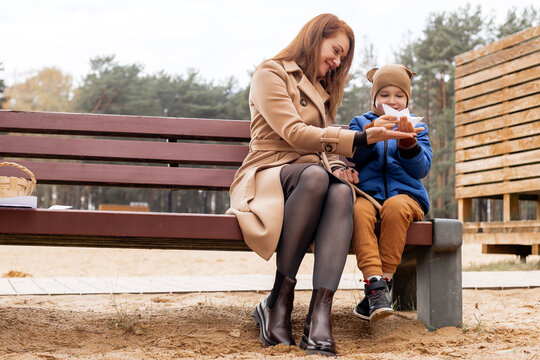 Happy Mother and Son Holding a Handmade Paper Boat Together in Autumn Park