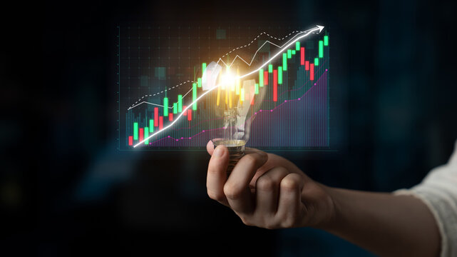 A person holds a light bulb in front of a vibrant stock market graph, symbolizing innovation and growth in finance and creative business solutions. Impute